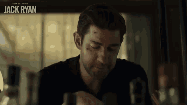 a man in a black shirt is sitting in front of a sign that says tom clancy 's jack ryan