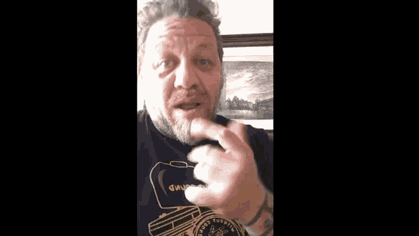 a man with a beard is giving the middle finger while wearing a black shirt .