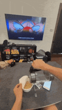 a person is sitting at a table with a bowl of food in front of a television