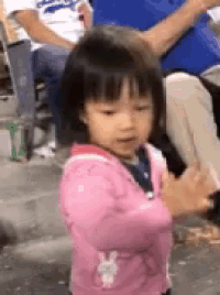 a little girl in a pink jacket is clapping her hands at a baseball game .