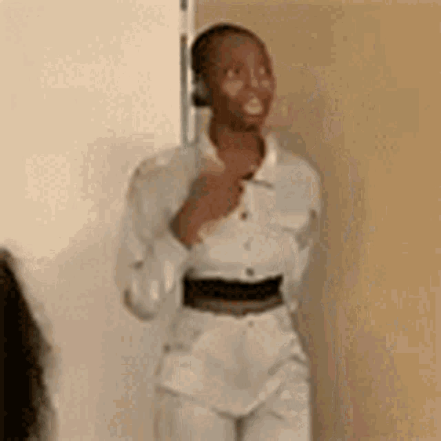 a woman in a white shirt and white pants is standing in front of a wall .