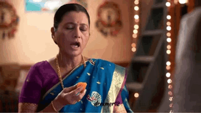 a woman in a blue and purple sari is eating a piece of food .