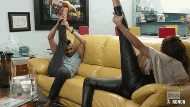 a man and a woman are stretching their legs on a yellow couch that says bravo a ronog