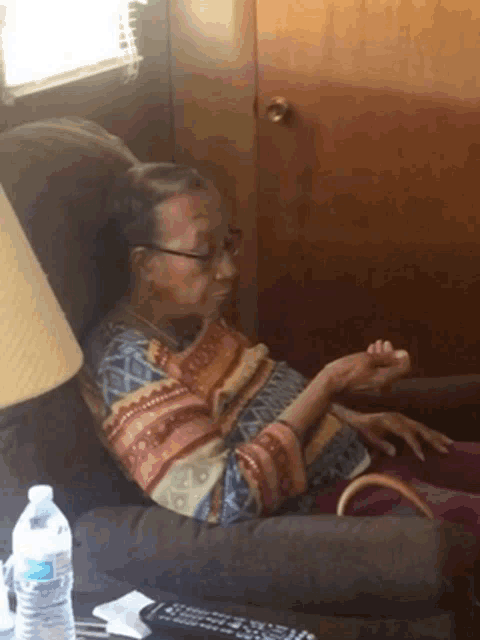an elderly woman sits in a chair with a bottle of aquafina water on the table