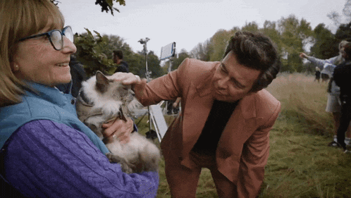 a man in a suit petting a cat while standing next to a woman