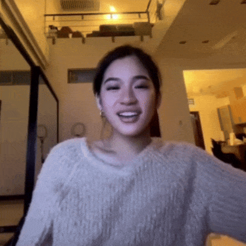 a woman in a white sweater is smiling in a room