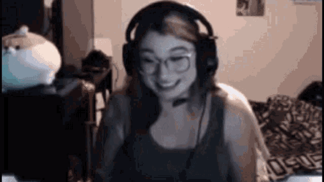 a woman wearing headphones and glasses is smiling in front of a computer screen .