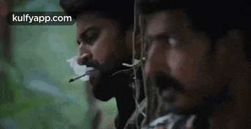 a man with a beard is smoking a cigarette in a forest .