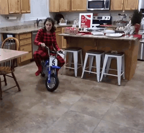 a woman is riding a motorcycle in a kitchen with a sign that says ' christmas ' on it