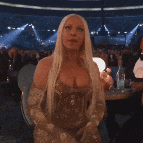 a woman with long blonde hair and a very large breast is sitting in front of a crowd .