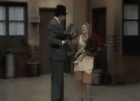 a man in a suit is standing next to a woman in an apron holding a bouquet of flowers .