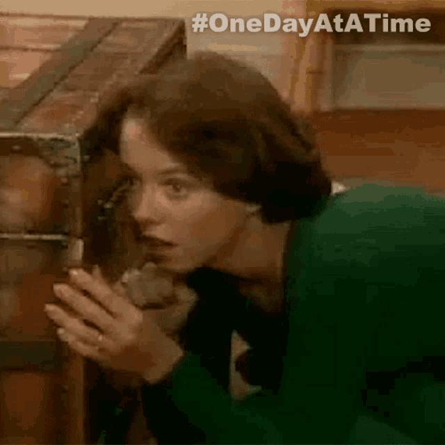 a woman in a green sweater is looking into a wooden trunk .