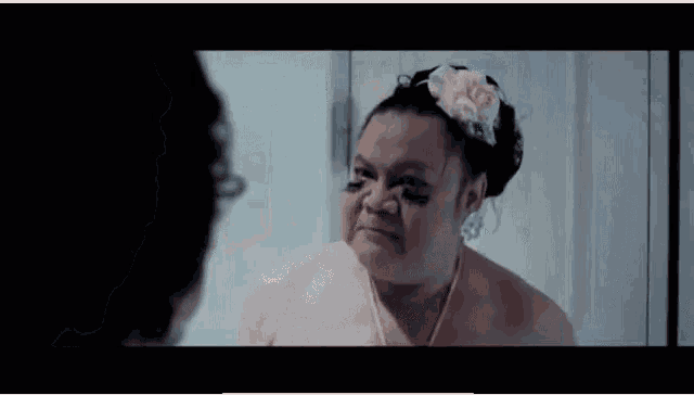 a woman with a flower in her hair looks at herself in the mirror