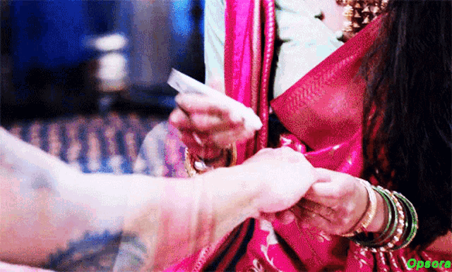 a woman in a pink saree is holding a piece of paper in her hand and the word opera is on the bottom right