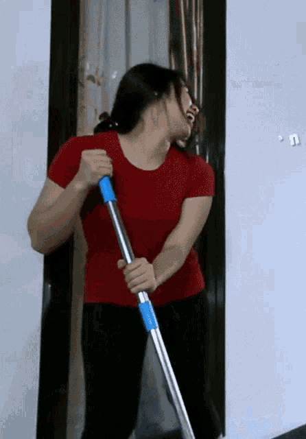 a woman in a red shirt is holding a mop and laughing