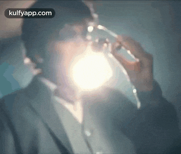 a man in a suit is drinking from a glass with a light behind him .