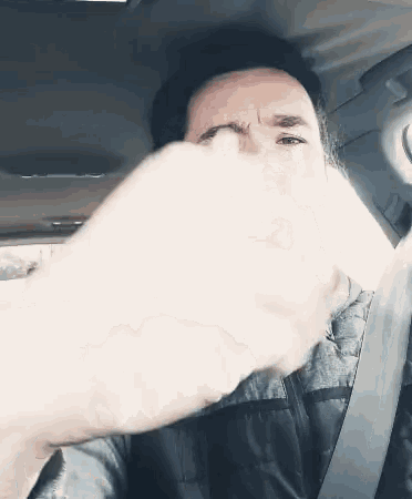 a man covering his face with his hand while sitting in a car