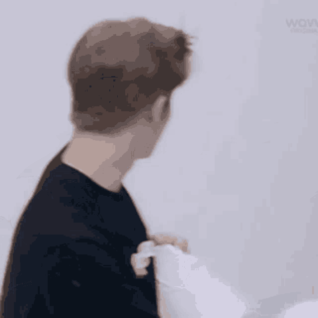a man in a black shirt is standing in front of a white wall holding a pillow .
