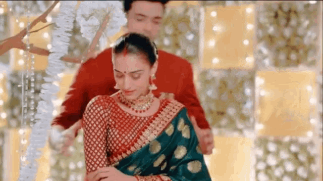 a man in a red suit is standing next to a woman in a green and gold saree