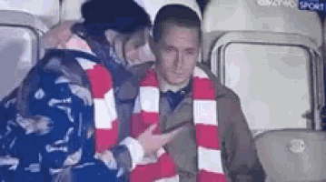 a man wearing a red and white scarf is being touched by a woman in a stadium .