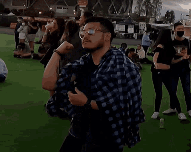 a man wearing sunglasses and a plaid shirt is standing in a crowd