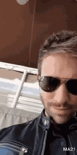 a man wearing sunglasses and a leather jacket has the number ma21 on the bottom right
