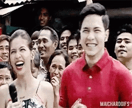 a man and a woman are laughing in front of a crowd while a man holds a microphone .
