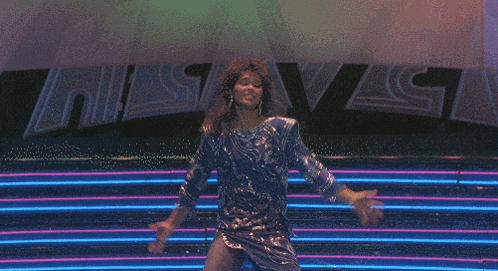 a woman in a blue dress is dancing in front of a neon sign that says heaven
