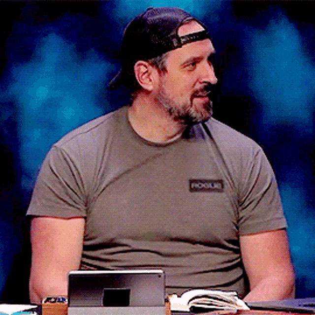 a man wearing a hat and a t-shirt that says fools is sitting at a desk