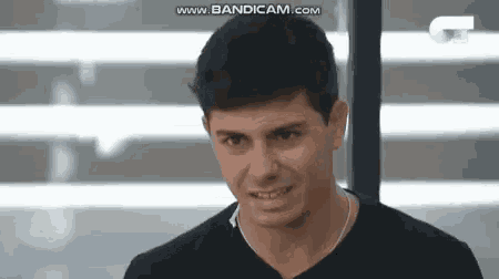 a young man in a black shirt is smiling and looking at the camera in front of a window .