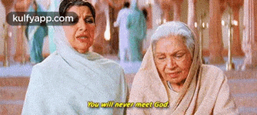 two older women are sitting next to each other in a room and talking .