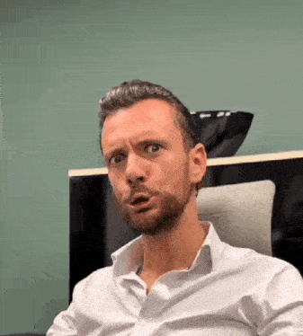 a man with a beard wearing a white shirt is making a funny face
