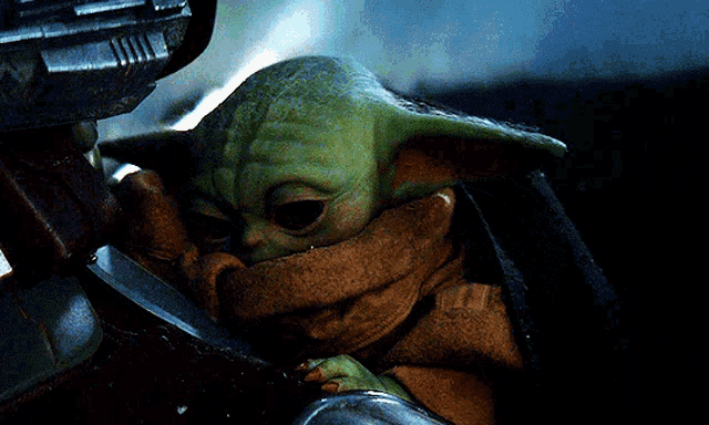 a baby yoda is laying in a blanket in a dark room with a gun in the background .