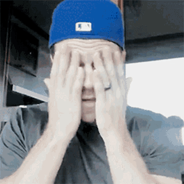 a man wearing a blue hat and a ring is covering his face