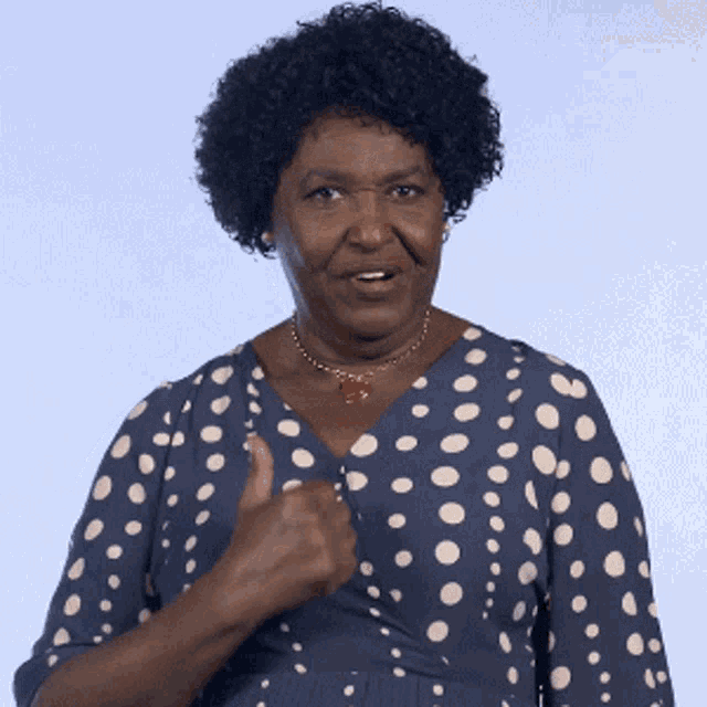 a woman wearing a blue and white polka dot dress holds her fist to her shoulder