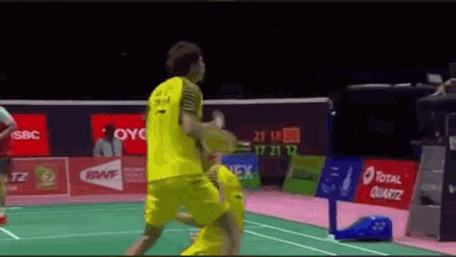 a man in a yellow shirt is playing badminton on a green court .