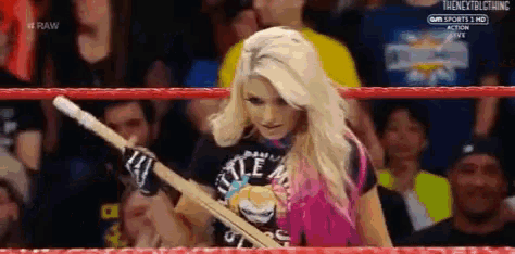a woman in a pink shirt is holding a stick in a wrestling ring .