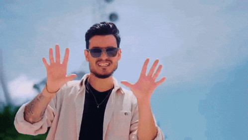 a man wearing sunglasses and a white shirt is making a funny face with his hands .