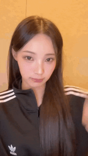 a young woman with long hair is wearing a black adidas jacket .