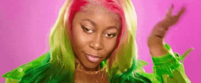 a woman with green and pink hair is wearing a green jacket and a gold sweater .