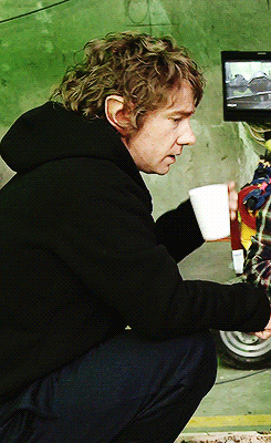 a man in a black hoodie is squatting down holding a cup of coffee
