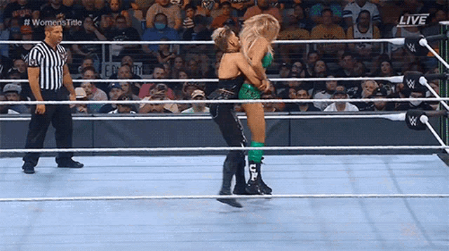 a woman is being lifted in a wrestling ring while a referee stands behind her