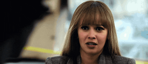a woman with bangs is wearing a plaid jacket and making a face .