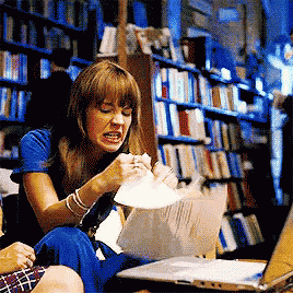 a woman in a blue shirt is sitting in front of a laptop in a library