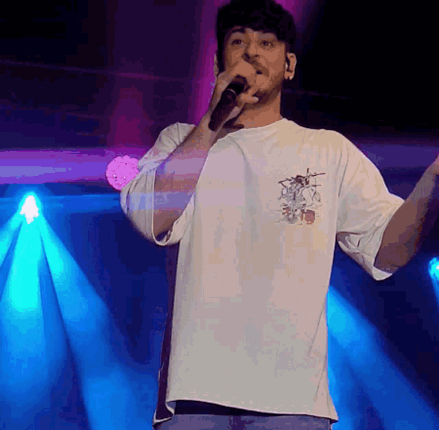 a man singing into a microphone while wearing a white shirt with a drummer on the back