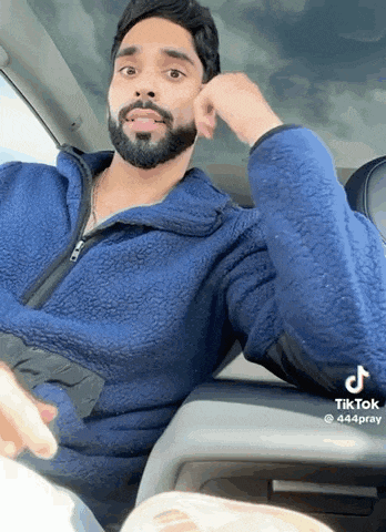 a man with a beard is sitting in the driver 's seat of a car wearing a blue jacket .