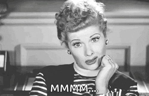 a black and white photo of a woman sitting at a table with her hand on her chin and a ring on her finger .