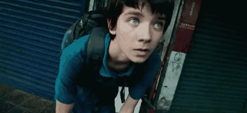a young boy in a blue shirt with a backpack looks up at something
