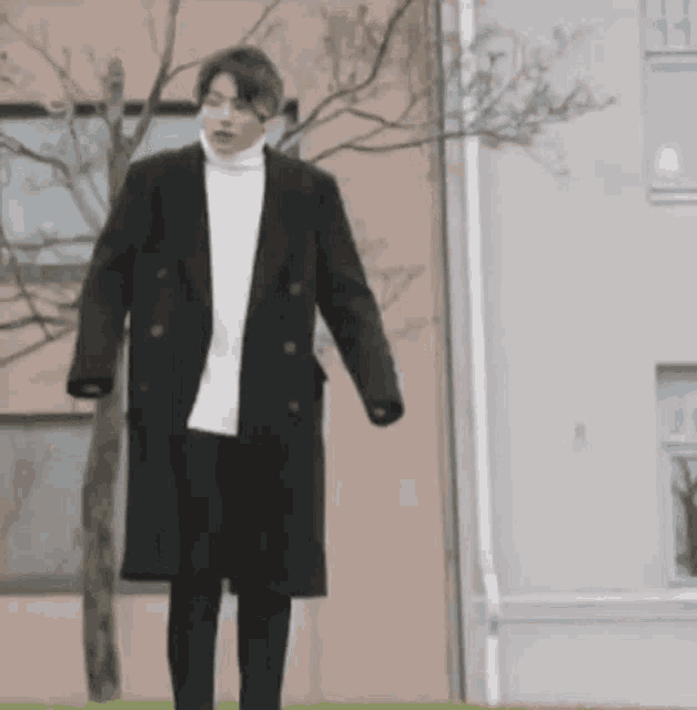 a man is standing in front of a building wearing a black coat and a white sweater .