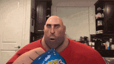 a bald man in a red shirt is holding a bag of chips